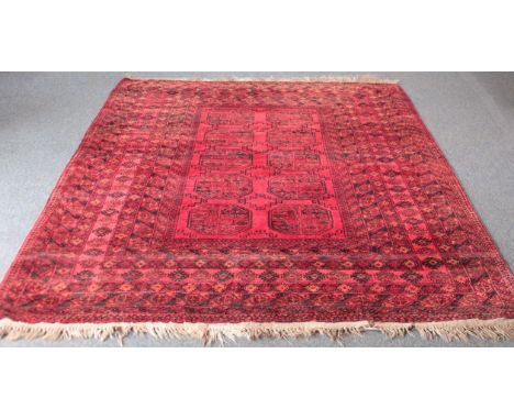A Bokhara hand-knotted wool rug - second half 20th century, the raspberry-red field with two rows of five octagonal gols, wit