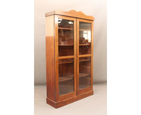 A 19th century mahogany glazed bookcase - the wavy cornice over two two-pane doors enclosing four removable shelves, raised o