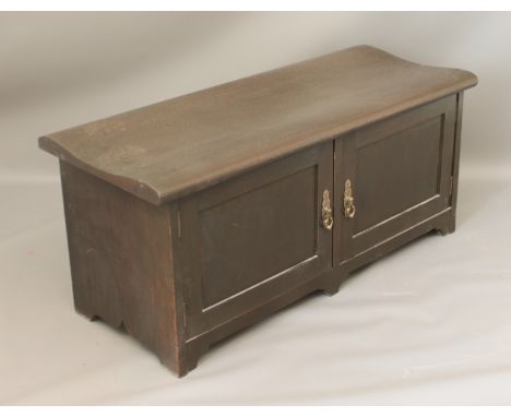 A stained oak bench-cupboard - the shaped top over two paneled doors enclosing two removable shelves. (LWH 99 x 41 x 43cm)