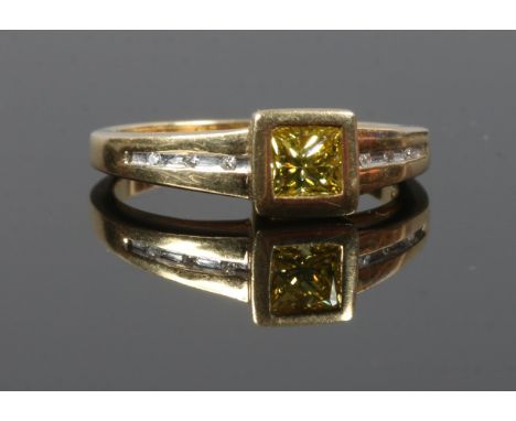 An 18ct gold ring set with a yellow Princess cut diamond and with channel set diamond shoulders, size N.