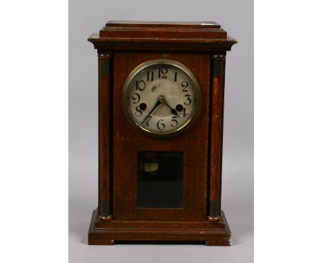 An oak cased eight day mantel clock with silvered dial and column supports with pendulum and key.