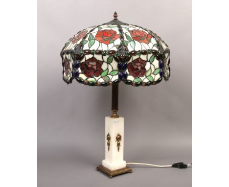 A Tiffany style table lamp with coloured leaded glass shade, raised on a brass and alabaster base.