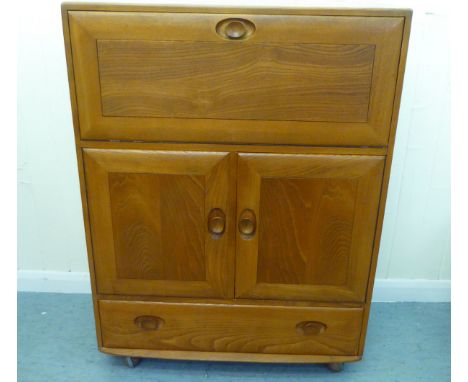 A blonde Ercol elm side cabinet with a fall flap, over two cupboard doors and a long drawer, on a plinth&nbsp; 44"h&nbsp; 32"