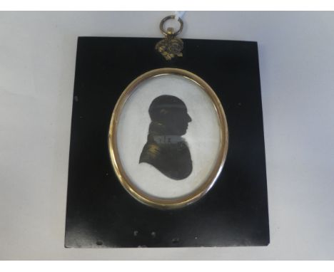 An 18thC oval profile head and shoulders portrait miniature, part gilded silhouette, featuring a gentleman wearing a topcoat,