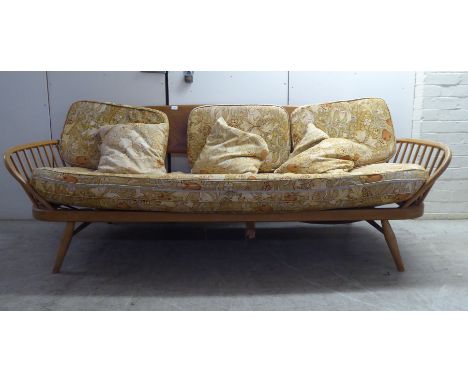 An Ercol blonde elm and beech framed daybed with a solid surfboard back and low hoop and spindled back ends, raised on ellipt