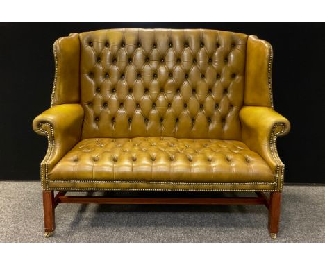 A George III style reproduction Chesterfield wing-back bench sofa, deep button back, pale tan leather, mahogany base, brass c