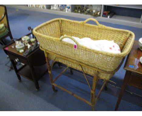 A caned wicker work Moses basket on a cane and bamboo stand, with bed linen, a mid 20th century mahogany two-tier trolley wit