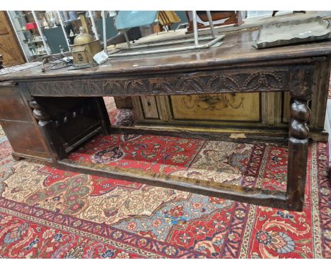 AN OAK REFECTORY TABLE, THE CLEATED PLANK TOP OVER APRONS CARVED ON THE LONG SIDES WITH ROUND ARCH FOLIAGE BANDS, THE LEGS AN
