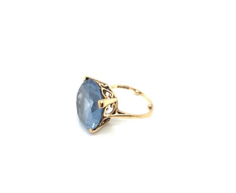 A 9ct HALLMARKED GOLD SYNTHETIC BLUE SPINEL COCKTAIL RING. THE LARGE STONE IN A RAISED FOUR CLAW SETTING WITH SCROLL GALLERY.