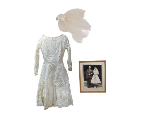 A 1956 short length wedding dress with 3/4 sleeves in a slub sateen fabric with bows decorating the skirt and a buckram under