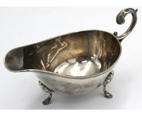 A George V silver sauceboat, with scrolled handle and upon three feet, hallmarked by William Hutton & Sons, Birmingham, 1913,