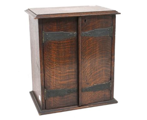 A 20th century oak tobacco stand and cupboard, with hinged doors revealing two above one drawers and lower revolving pipe and
