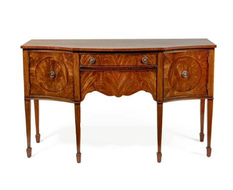 The serpentine crossbanded top above two short graduated drawers flanked by doors, each enclosing a shelf, on square-section 