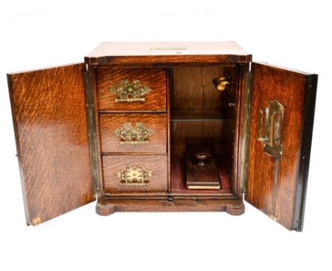 An Edwardian oak stationary and smokers cabinet, the brass mounted and molded double doors opening to reveal a fitted interio