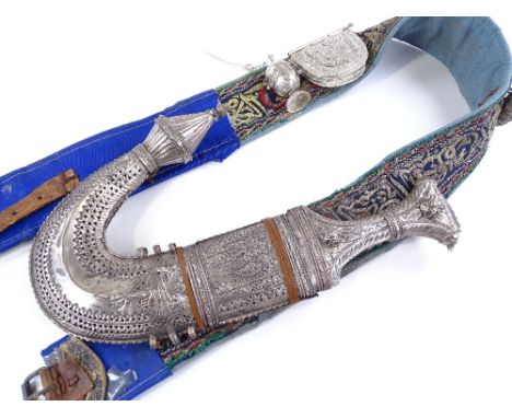 A Middle Eastern jambiya knife, with ornate white metal mounts and scabbard, complete with embroidered belt