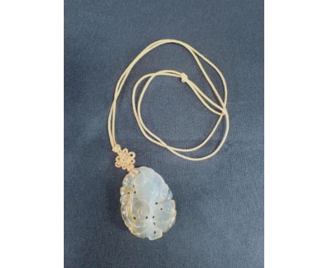 A CARVED JADE PENDANT carved with flowers and fruit, 4.5cm long, on plaited orange cord