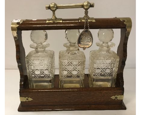 An early 20th Century oak three bottle tantalus containing three hobnail cut bottles, a Queen Elizabeth II Silver Jubilee win