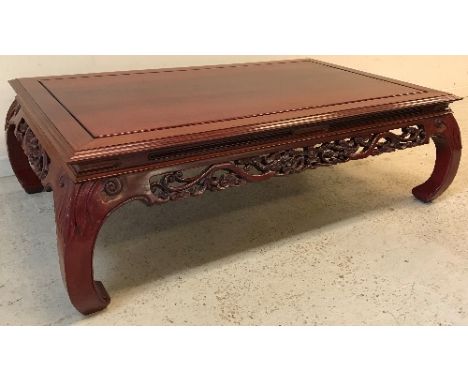 A modern Chinese cherry wood coffee table, the plain top with moulded edge over a dragon and blossom fretwork carved frieze, 