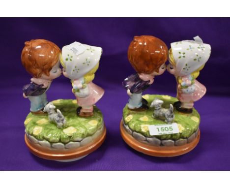 A pair of mid-century pottery figurines in the manner of Hummel, two kissing children with rotating musical stands