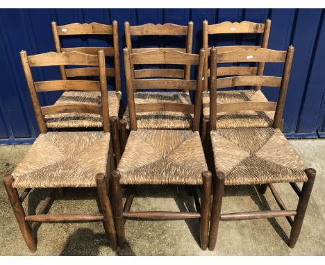 A set of six Gordon Russell Cotswold School dining chairs in oak with rush seats and ladder backs bearing copper labels to un