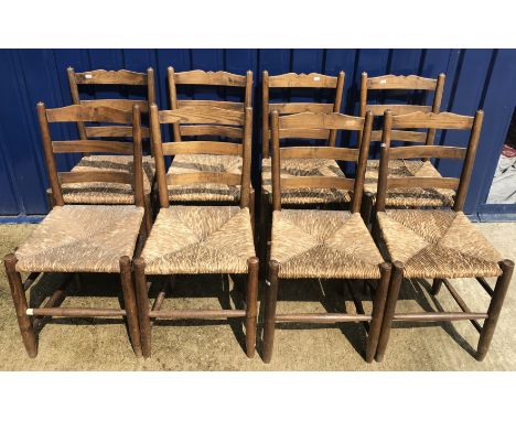 A set of eight Gordon Russell Cotswold School dining chairs in oak with rush seats and ladder backs bearing copper labels to 