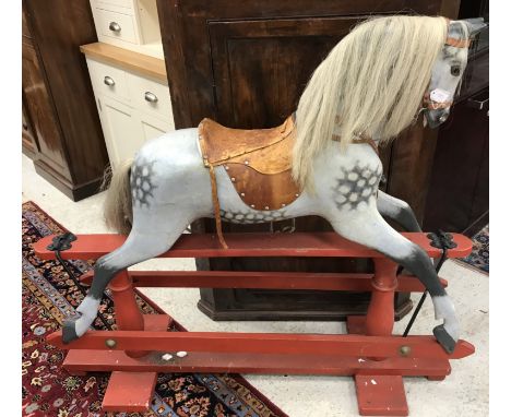 A vintage dapple painted grey wooden rocking horse with hair mane and tail and studded leather thin saddle on a red painted w