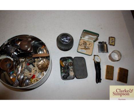 A tin of various costume jewellery, napkin rings, table lighter etc.