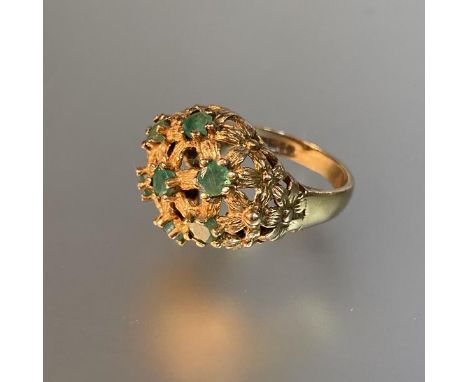 A 1970's emerald dress ring, the domed textured basketweave plaque set with seven emerald points, on a 9ct yellow gold band. 