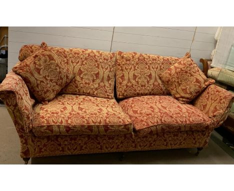 A three seater sofa with floral red and gold coloured upholstery on brass castors (H86cm W230cm D94cm)