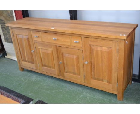 A modern light oak sideboard, rectangular top, long drawer over two fielded panel door cupboard flanked by conforming cupboar