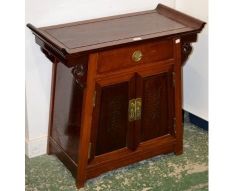 A Chinese hardwood altar cabinet, rectangular top with scroll ends above a drawer and a pair of doors, carved in relief with 
