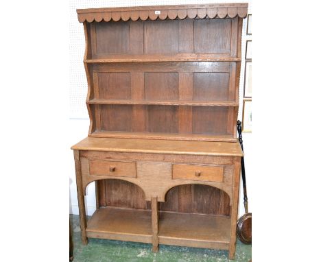A Cotswold School oak dresser, wavy frieze above two shelves knulled and carved with arcs, the projecting base with a pair of