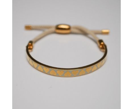 Halcyon Days enamel and cord bracelet featuring a gold-plated half-bangle with a soft cream enamel inlay adorned with a repea