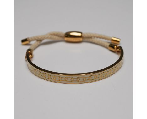 Halcyon Days gold-plated bracelet featuring a sleek half-bangle design with an intricate cream enamel pattern. The bracelet i