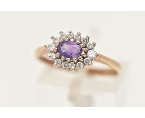 A 9CT YELLOW GOLD AMETHYST CLUSTER RING, of an oval form, set to the centre with an oval cut amethyst within a surround of ci