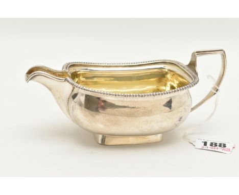 A GEORGE III SILVER MILK JUG, polished rectangular form with gadrooned rim, engraved crest to one side, with handle and gilt 