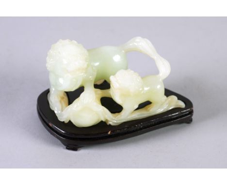 A MODERN ORIENTAL GREEN JADE CARVING OF A BUDDHISTIC LION AND PUP  PLAYING WITH A BROCADED BALL on wooden stand 