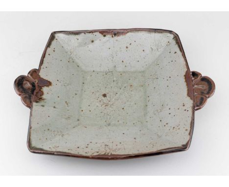 † PHIL ROGERS (1951-2020); a large square stoneware twin handled dish covered in green ash and tenmoku breaking to kaki glaze