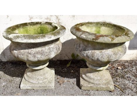 A pair of reconstituted stone twin handled garden urns, with egg and dart moulded rims and scrolling acanthus leaf detail, on