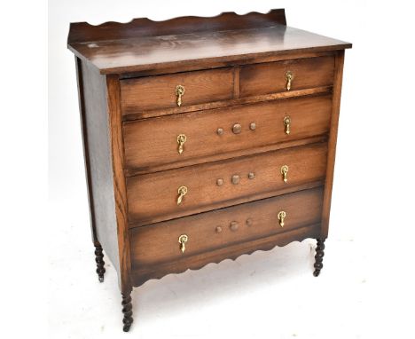 A 1920s oak chest of drawers with wavy gallery back above two short over three long drawers, raised on turned column supports