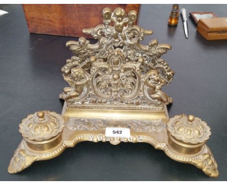 AN EARLY 20TH CENTURY BRASS DESK STAND WITH INKWELLS, highly embossed, along with a brass table lighter and an ashtray.