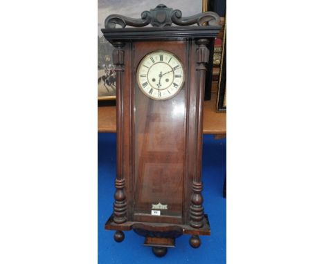 A LARGE WALNUT WALL CLOCK with a white enamelled face with roman numerals (lacking pendulum).