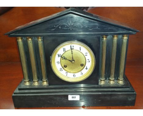 A BLACK SLATE MANTEL CLOCK OF SIMPLE FORM with a brass bezel, white enamel and brass face flanked by three brass pillars eith