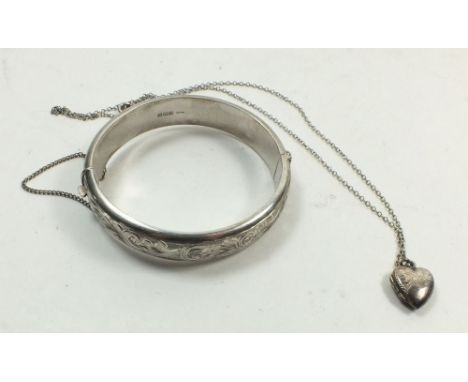 A silver engraved bangle and a silver small heart form locket on chain 