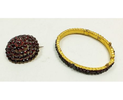 A late 19th century gilt metal Bohemian garnet cluster brooch (one stone missing) along with a garnet set metal bangle (some 