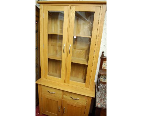 A contemporary light oak bookcase cupboard having twin door glazed upper section, width 98cm