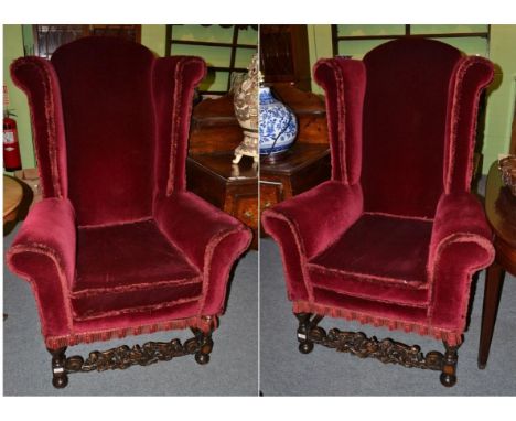 < A pair of Queen Anne style wingback chairs, late 19th/early 20th century, upholstered in red velvet, with overstuffed arms 