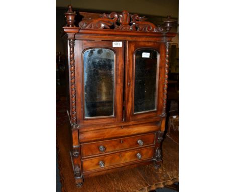 A miniature Victorian mahogany clothes press, circa 1850, with mirrored doors enclosing sliding trays, all between spiral tur