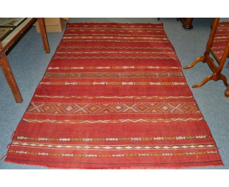 A Moroccan flat weave carpet, North West Africa, the madder field with narrow bands of polychrome geometric designs, 310cm by