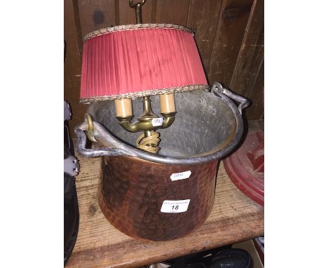 A hammered copper jam pot with handle and a brass table lamp. 